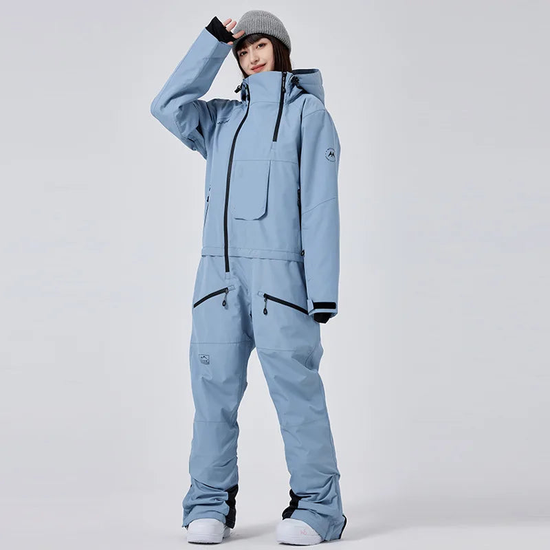 Frau in hellblauem Skianzug mit Kapuze und grauer Mütze, steht aufrecht. Wintermode, Outdoor-Bekleidung, Skibekleidung für Damen.