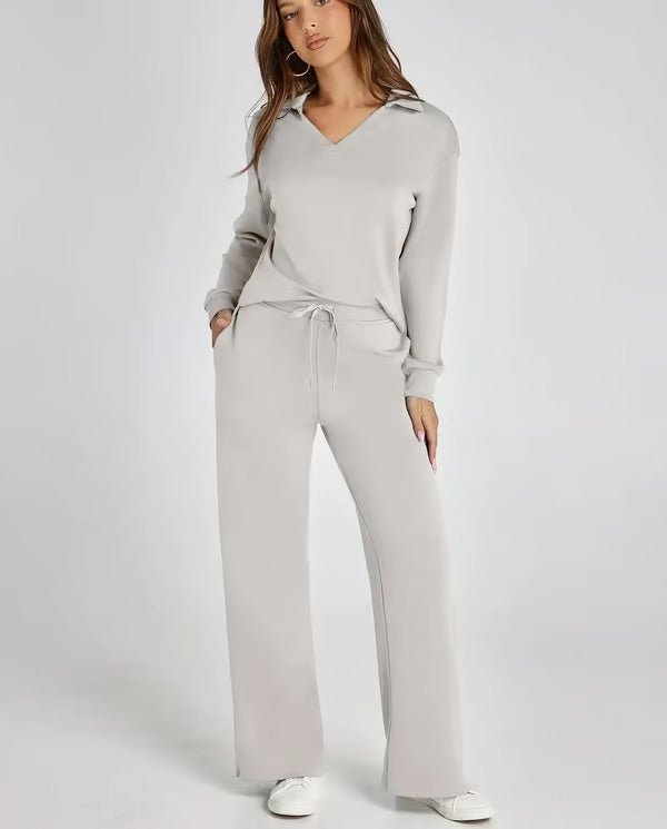 Frau in grauem Lounge-Set mit V-Ausschnitt und Kordelzughose, lässig und bequem, modisches Freizeitoutfit, weiße Sneaker, Studiohintergrund.