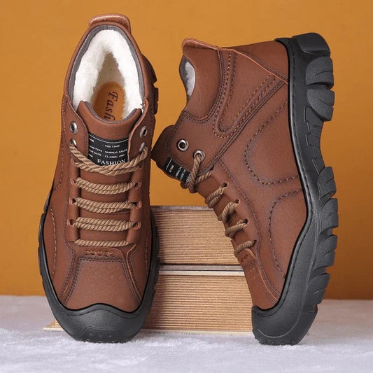 Braune Herren-Winterstiefel mit schwarzer Sohle, warm gefüttert, auf Holzkiste vor orangefarbenem Hintergrund. Robuste Outdoor-Schuhe.