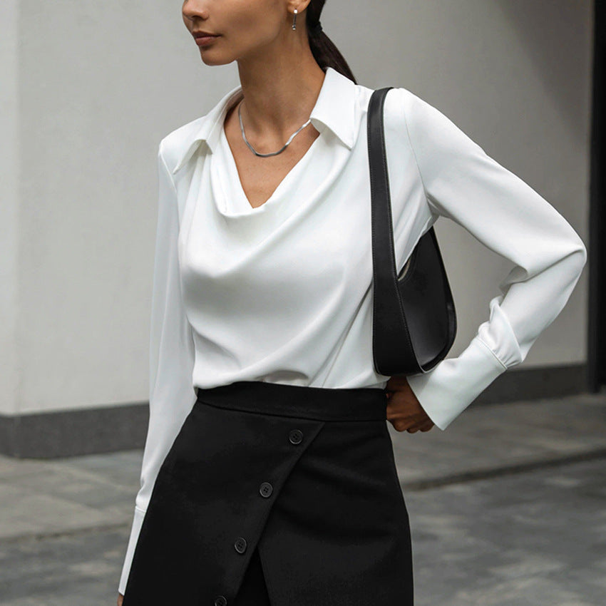 Frau in eleganter weißer Bluse und schwarzem Rock, trägt schwarze Schultertasche. Businessmode, stilvoll, modern, Büro-Outfit.