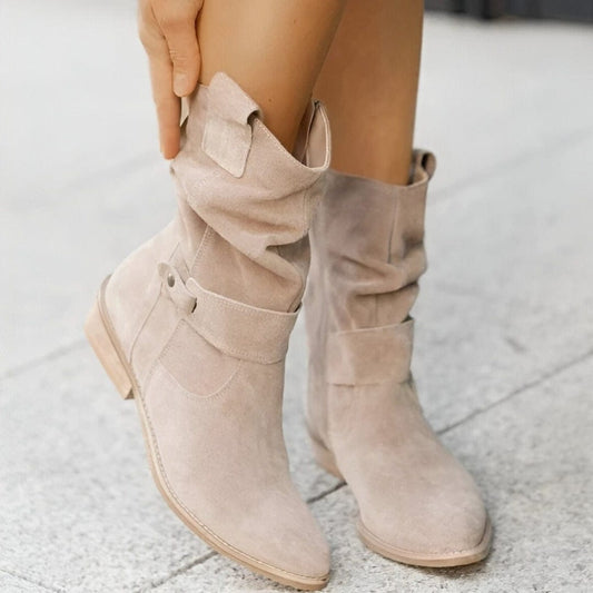 Beige Wildlederstiefel mit flachem Absatz, lässigem Design und Riemendetails auf grauem Boden. Perfekt für Herbstmode und stilvolle Outfits.