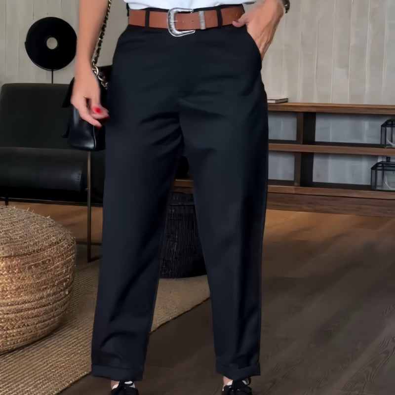 Elegante schwarze Hose mit braunem Gürtel, getragen von einer Person in modernem Wohnzimmer. Stilvolle Damenmode, Freizeitlook, Innenraum.
