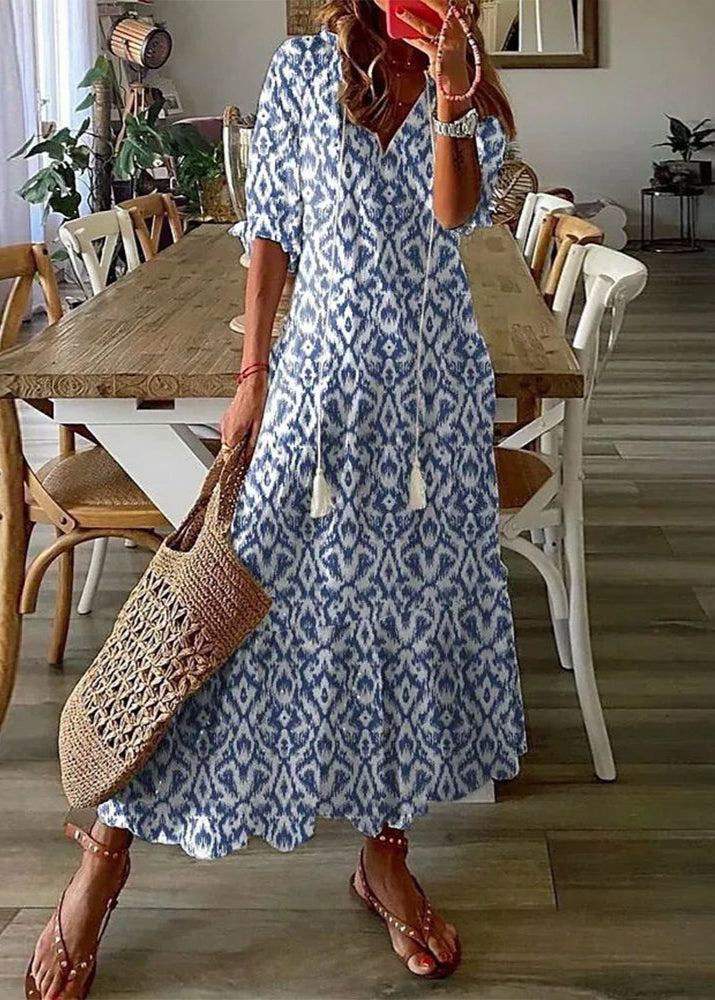 Frau in blau-weißem Ikat-Musterkleid, hält eine geflochtene Tasche, steht in modernem Esszimmer mit Holztisch und weißen Stühlen.