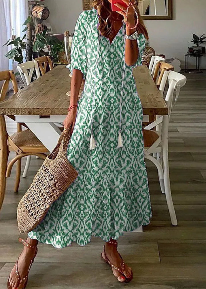 Frau in grün-weißem Ikat-Musterkleid, hält eine geflochtene Tasche, steht in modernem Esszimmer. Sommermode, Boho-Stil, Freizeitkleidung.