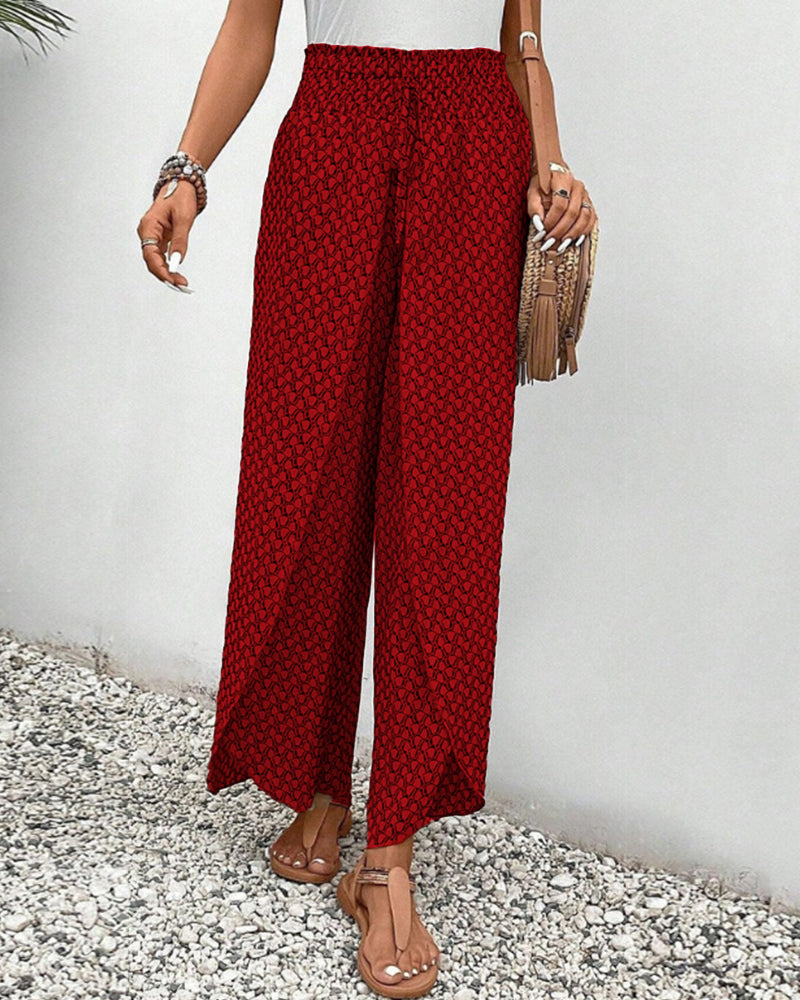 Frau in roter, gemusterter Hose und Sandalen, hält eine Fransenhandtasche. Sommermode, lässiger Stil, Damenbekleidung, modische Accessoires.
