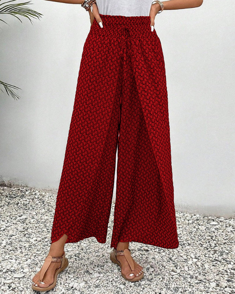 Frau trägt rote, gemusterte Palazzo-Hose, steht auf Kiesboden. Sommermode, weite Hosen, lässiger Stil, bequeme Damenbekleidung.
