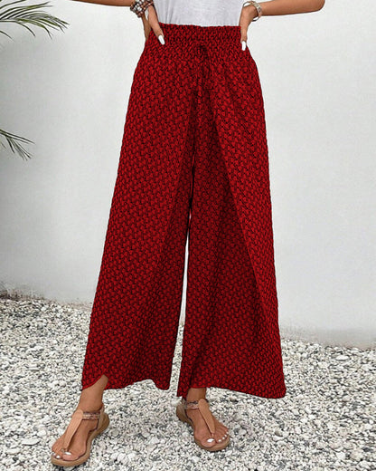 Frau trägt rote, gemusterte Palazzo-Hose, steht auf Kiesboden. Sommermode, weite Hosen, lässiger Stil, bequeme Damenbekleidung.
