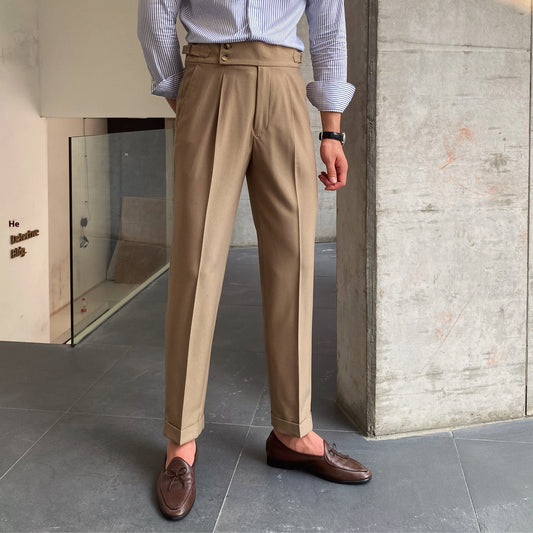 Mann in beigen Anzughosen, blauem Hemd und braunen Loafern steht in modernem Innenraum. Elegante Herrenmode, Business-Look, stilvolle Kleidung.