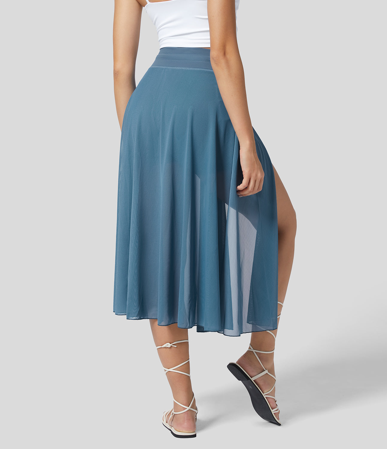 Frau in blauem, fließendem Midirock mit hohem Schlitz, weißem Top und Sandalen. Elegante Sommermode, stilvoller Look, Rückansicht.