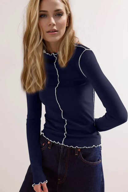 Blonde Frau in dunkelblauem Langarmshirt mit weißen Nähten und blauen Jeans. Modetrend, Damenbekleidung, stilvolles Outfit, Freizeitlook.