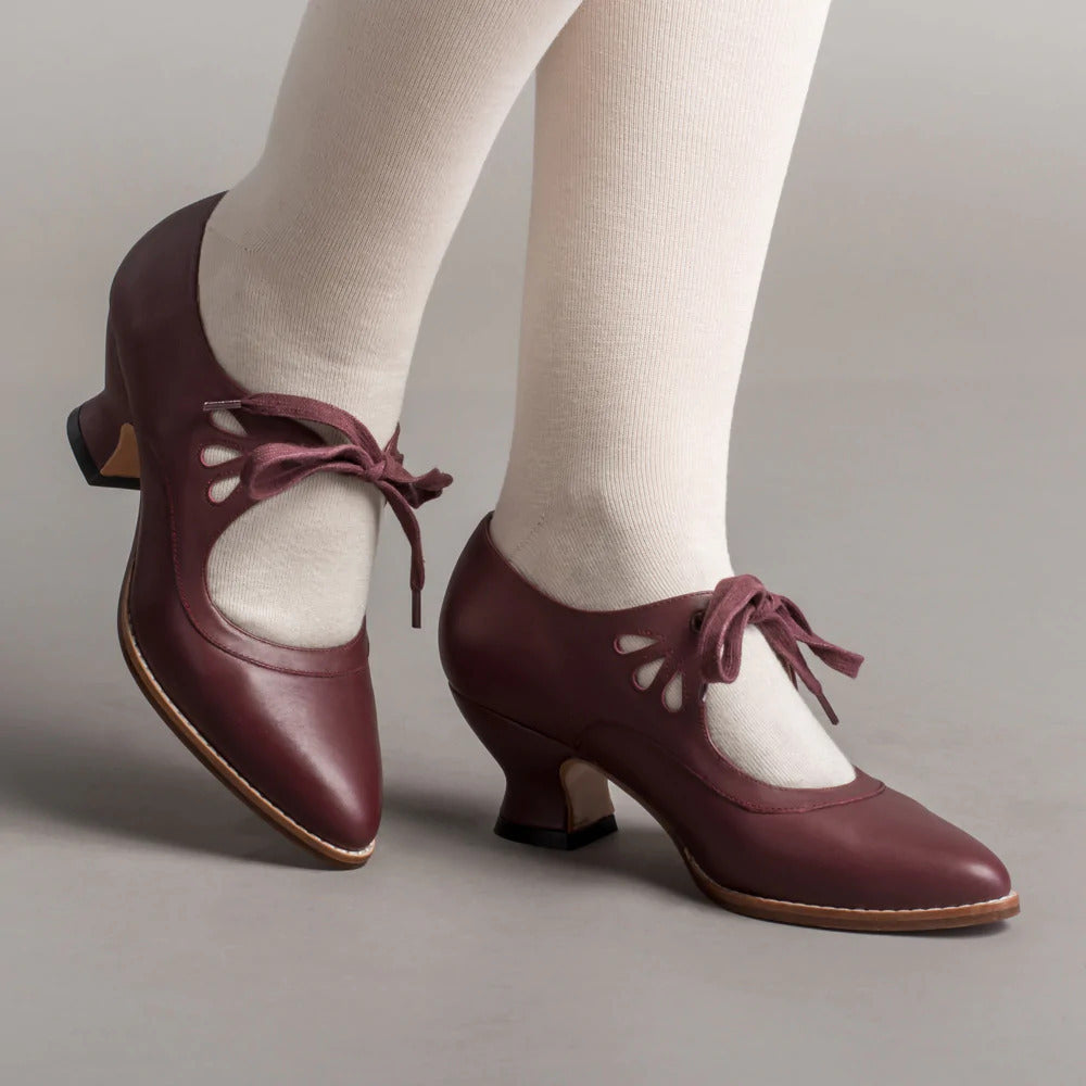 Braune Vintage-Damenschuhe mit Absatz und Schleifen, getragen mit weißen Strumpfhosen. Retro-Design, eleganter Look, ideal für klassische Mode.
