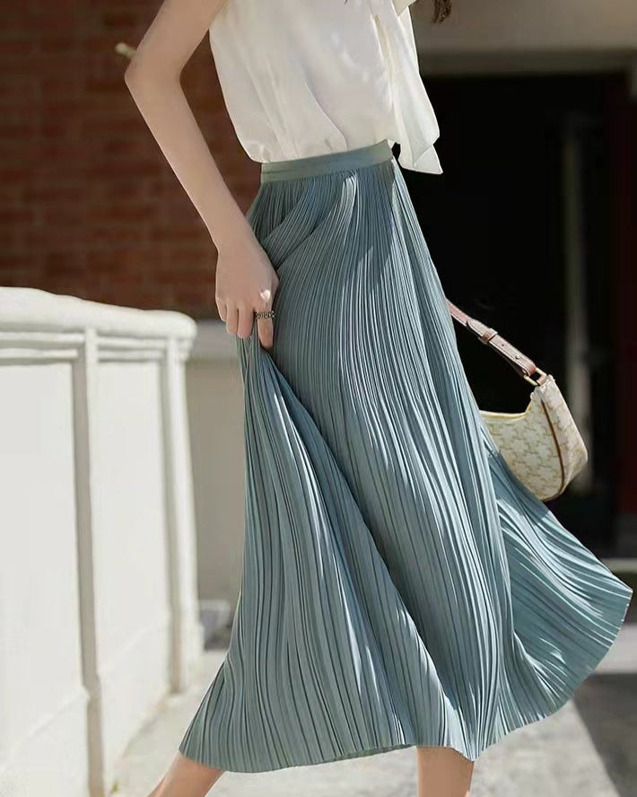 Frau in weißer Bluse und blauem Plisseerock, trägt eine beige Handtasche. Elegante Mode, Sommeroutfit, stilvoller Look.