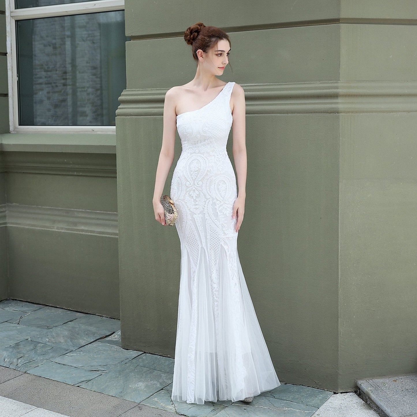 Frau in elegantem, einarmigem weißen Abendkleid mit Spitzenmuster, steht vor grüner Wand. Perfekt für formelle Anlässe und Hochzeiten.