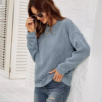 Frau in blauem Pullover und Jeans lehnt lächelnd an weißer Wand, trägt Sonnenbrille. Modetrend, lässiger Look, Damenmode, Freizeitkleidung.
