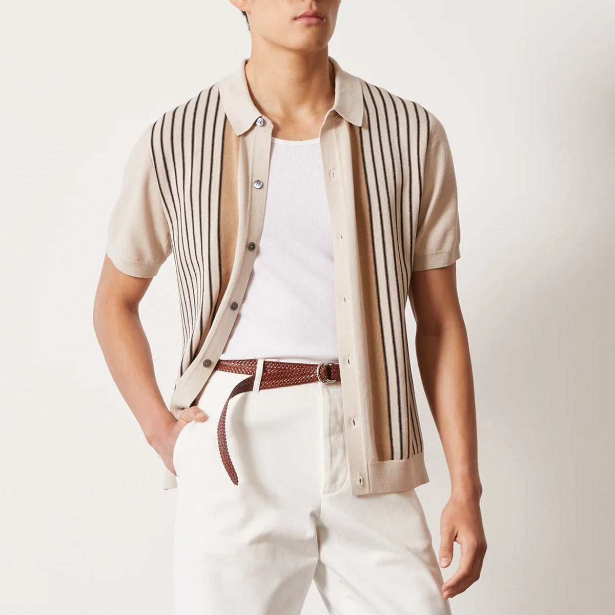 Mann trägt beige Strickhemd mit Streifen, weißes T-Shirt und weiße Hose. Modischer Sommerlook, Herrenmode, eleganter Freizeitstil.