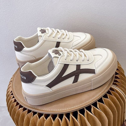 Weiße Sneaker mit braunen Details auf modernem, gefaltetem Kartonhocker. Modische Turnschuhe, Lederoptik, trendiges Design, bequeme Sohle.