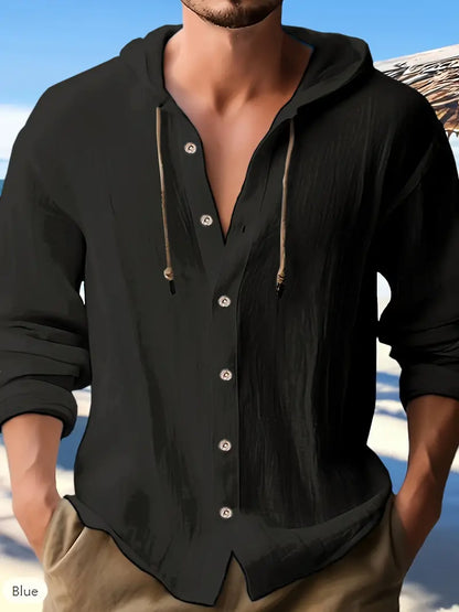 Mann in schwarzem Leinenhemd mit Kapuze und Knöpfen am Strand. Sommermode, Herrenbekleidung, lässiger Stil.