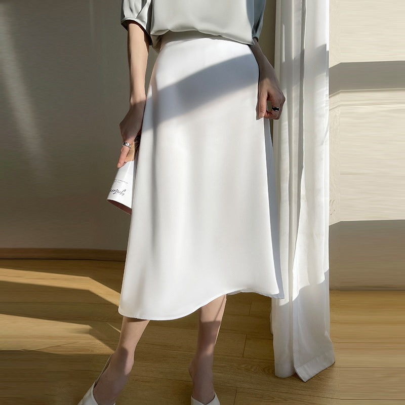 Eleganter weißer Midirock aus Satin, getragen von einer Frau in einem hellen Raum. Perfekt für Sommermode und stilvolle Outfits.