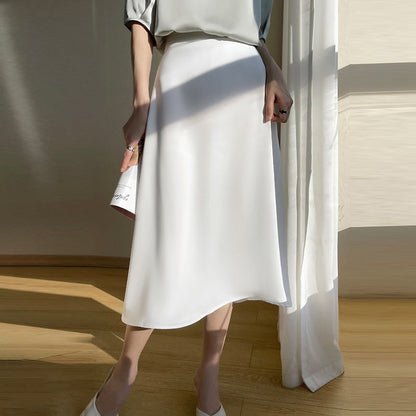 Eleganter weißer Midirock aus Satin, getragen von einer Frau in einem hellen Raum. Perfekt für Sommermode und stilvolle Outfits.