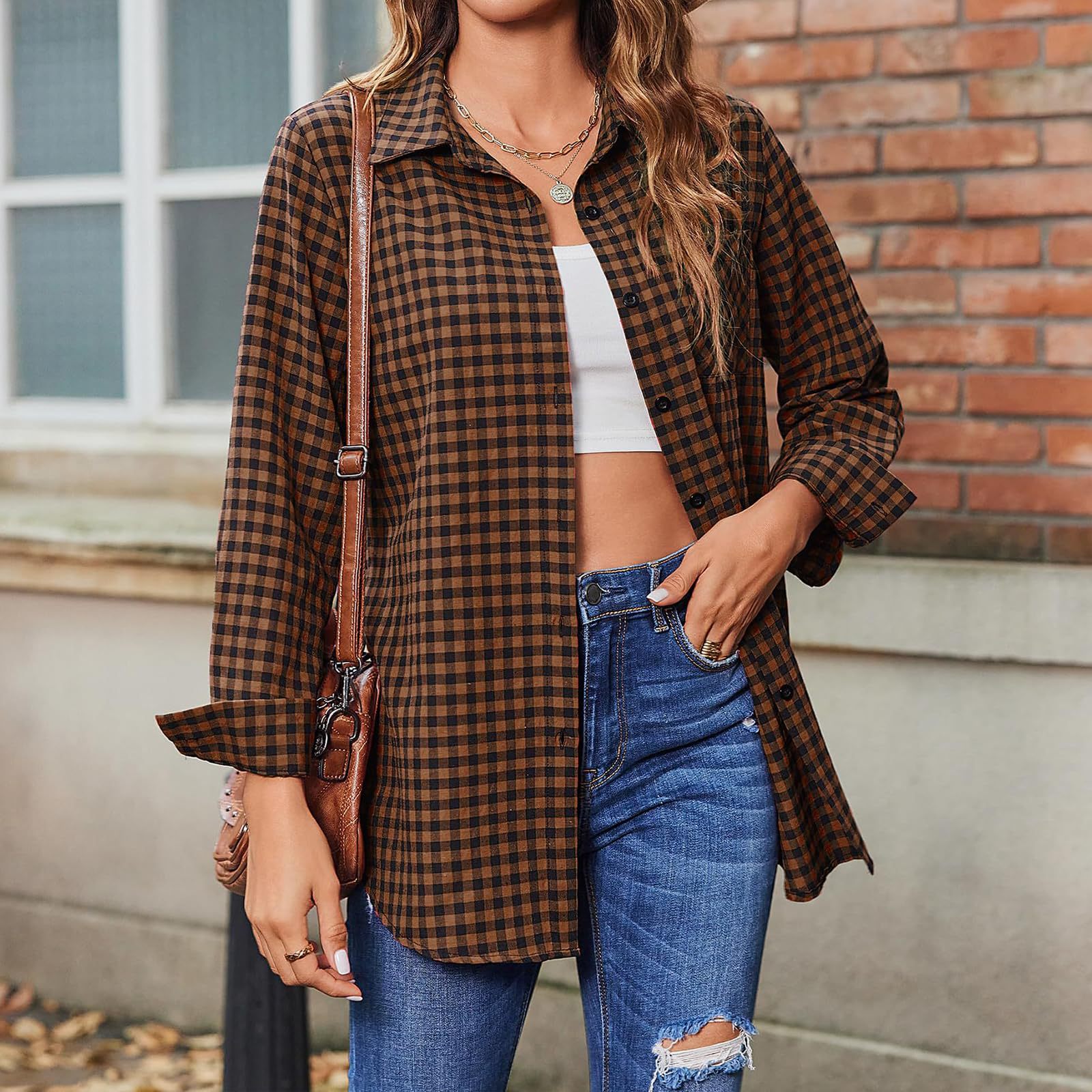 Frau in kariertem Hemd, weißem Crop-Top und blauen Jeans vor Backsteinwand. Modetrend, lässiger Stil, Herbstmode, Streetwear-Look.