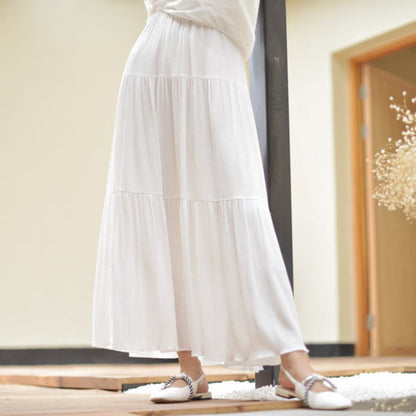 Frau in langem, weißem Maxikleid und flachen Schuhen steht in modernem Innenraum. Elegantes Sommeroutfit, Mode, Damenbekleidung.