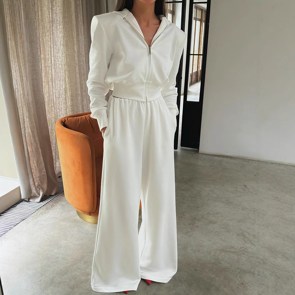 Frau in elegantem weißen Jumpsuit mit Reißverschluss, steht in modernem Wohnzimmer. Modetrend, stilvolle Damenbekleidung, minimalistisches Design.