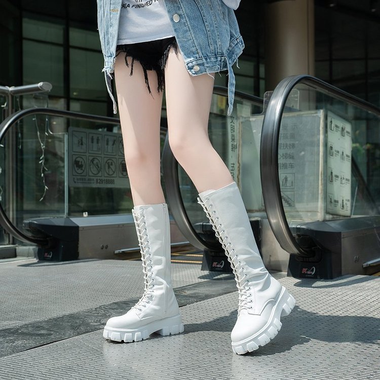 Frau in weißen Stiefeln und Jeansjacke auf Rolltreppe. Modische Damenstiefel, urbaner Stil, trendige Kleidung, Straßenmode.