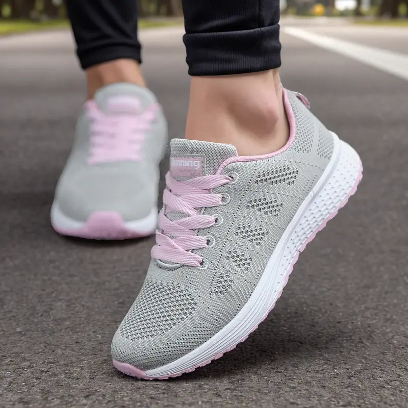 Graue Damen-Laufschuhe mit rosa Schnürsenkeln auf Asphalt. Atmungsaktives Mesh-Design, ideal für Fitness und Outdoor-Aktivitäten.