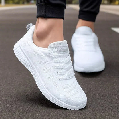Weiße Sportschuhe auf Asphalt, getragen von einer Person in schwarzer Sporthose. Bequeme, atmungsaktive Sneaker für Laufen und Fitness.