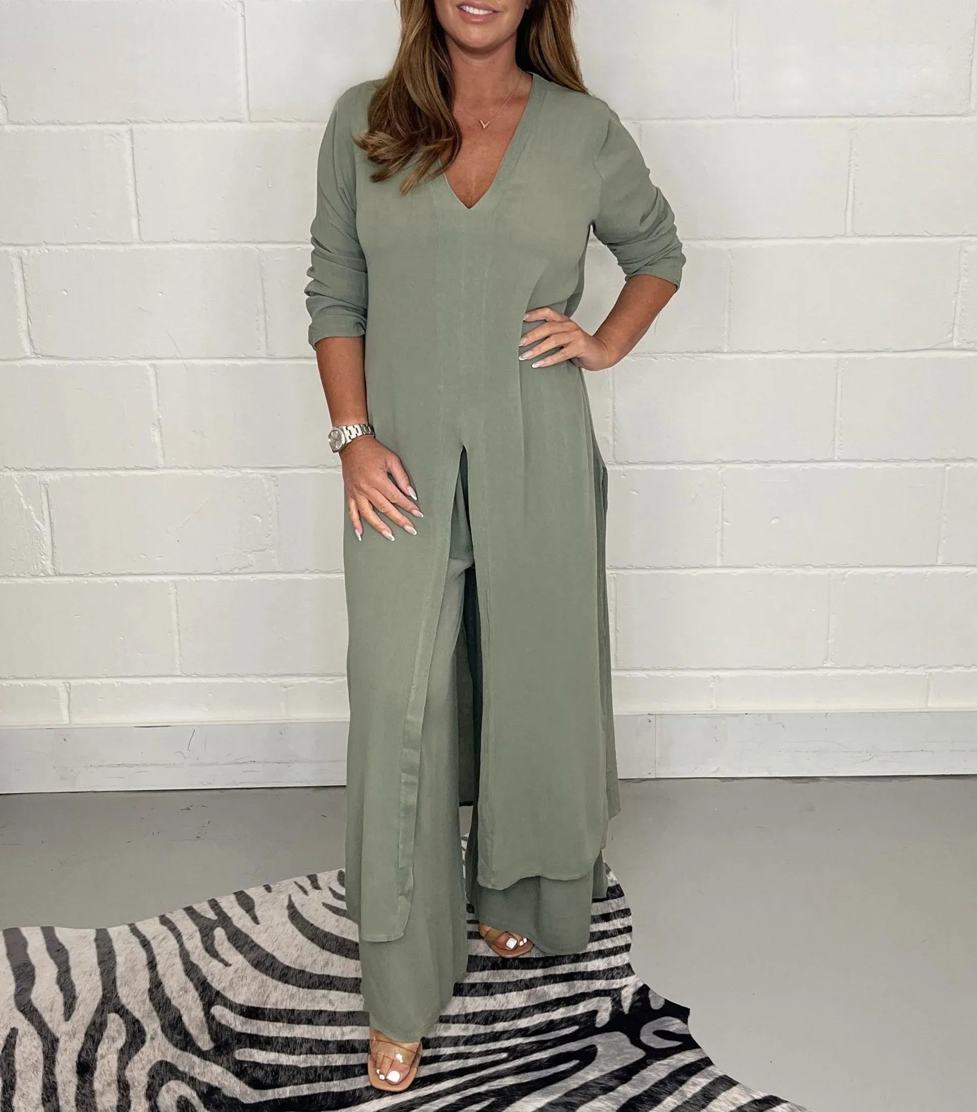 Frau in olivgrünem, langem Kleid mit V-Ausschnitt und Schlitz, steht auf grauem Boden mit Zebrateppich. Elegante Mode, lässiger Stil.