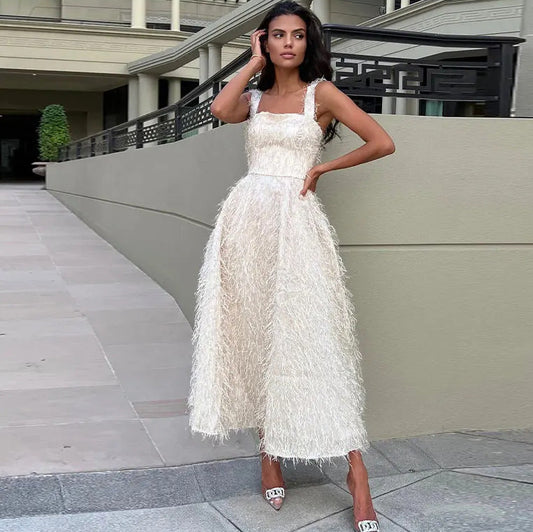 Frau in elegantem, weißem Abendkleid mit Fransen steht vor modernem Gebäude. Mode, Abendgarderobe, stilvolle Kleidung, luxuriöses Design.