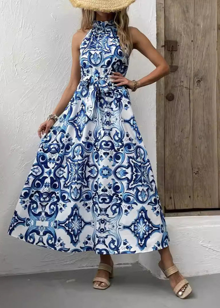 Frau in blau-weißem, gemustertem Maxikleid mit Strohhut vor Holztür. Sommermode, elegantes Design, Freizeitkleidung.