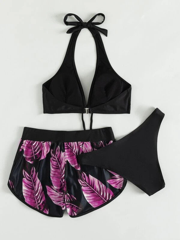 Damen-Bikini-Set mit schwarzem Neckholder-Oberteil, schwarzem Slip und tropisch bedruckten Shorts mit pinken Blättern, ideal für den Sommer.