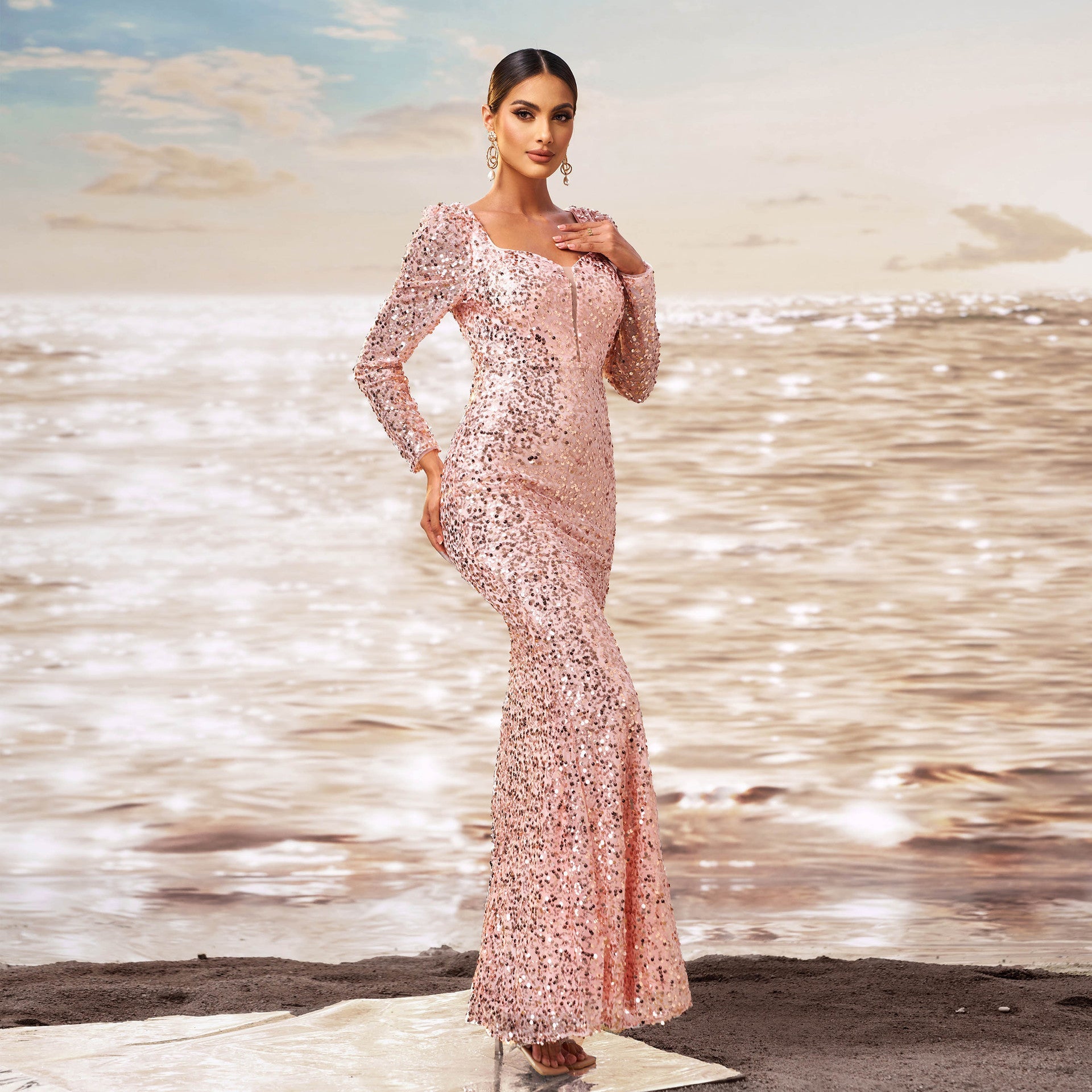 Elegantes Abendkleid in Roségold mit Pailletten, getragen von einer Frau am Strand bei Sonnenuntergang. Glamouröse Mode, Meereshintergrund.