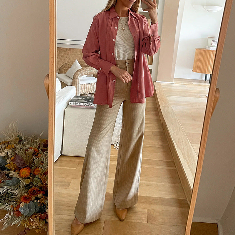 Frau in beiger Hose und rosa Hemd posiert vor einem Spiegel in modernem Wohnzimmer. Mode, Outfit, Innenarchitektur, Herbstdeko.