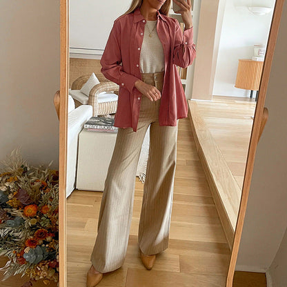 Frau in beiger Hose und rosa Hemd posiert vor einem Spiegel in modernem Wohnzimmer. Mode, Outfit, Innenarchitektur, Herbstdeko.
