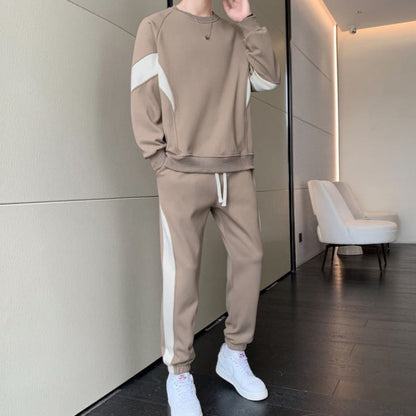 Person in beigem Trainingsanzug mit weißen Streifen, steht in modernem Raum. Sportbekleidung, Freizeitmode, Sneakers, Innenraum.