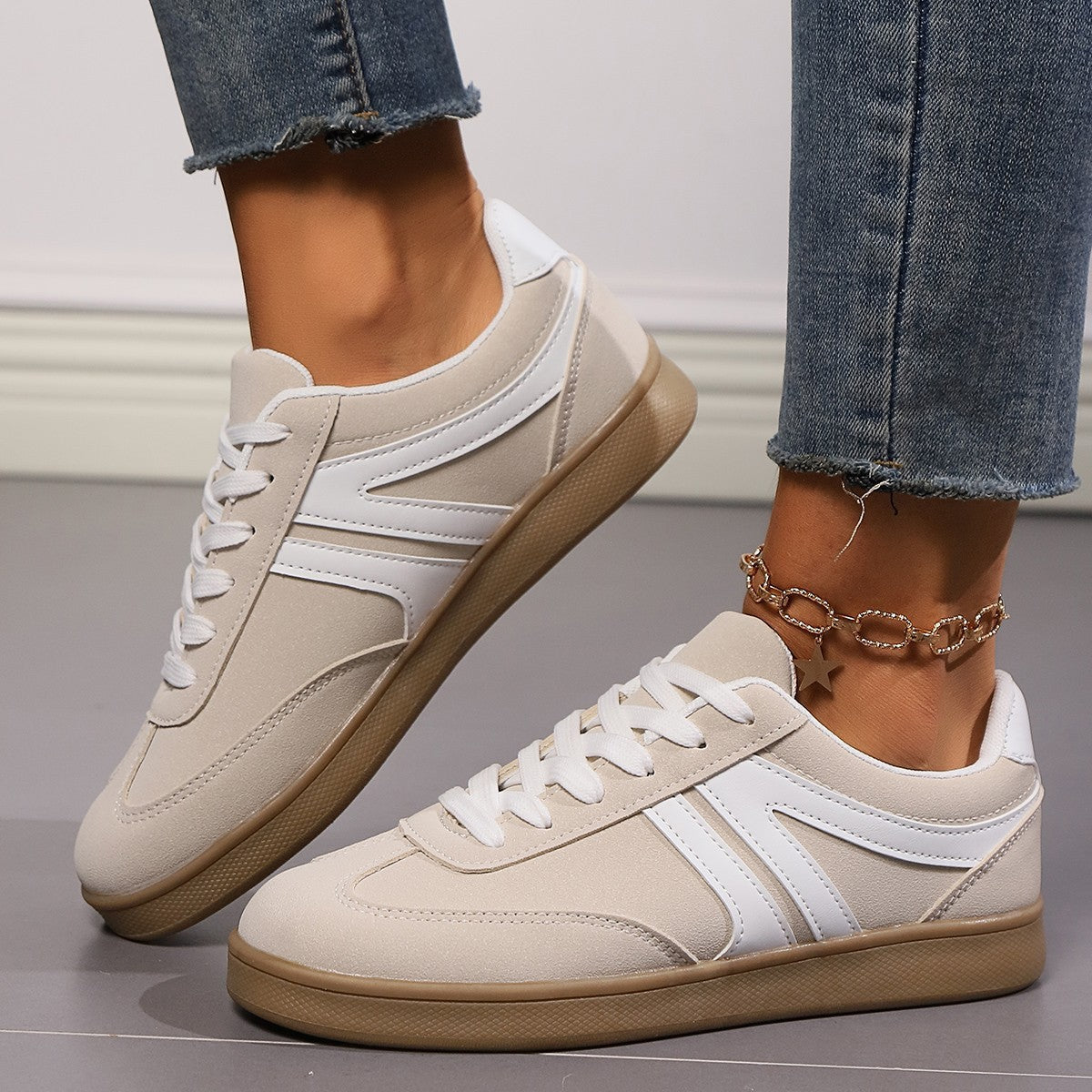 Damen Sneaker in Beige mit weißem Streifen, Gummisohle und Schnürsenkeln, getragen mit Jeans. Modische Freizeitschuhe für Alltag und Sport.
