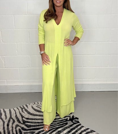 Frau in gelbem, langem Jumpsuit vor weißer Wand, trägt Armbanduhr, steht auf Zebrateppich. Modetrend, Damenmode, eleganter Look.