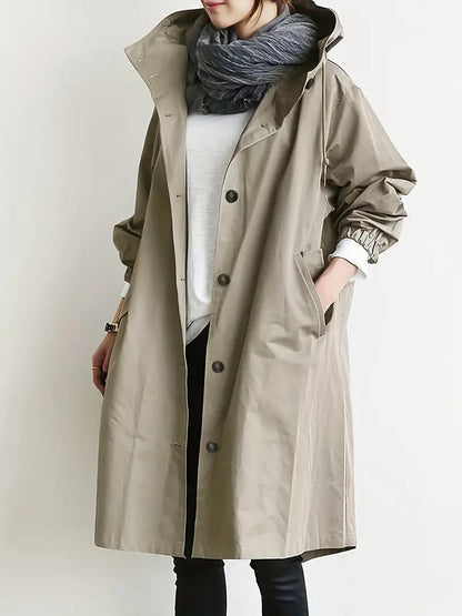 Frau trägt beigen Trenchcoat mit grauem Schal, weißem Shirt und schwarzer Hose. Modischer Herbstlook, Damenmode, stilvoller Mantel.