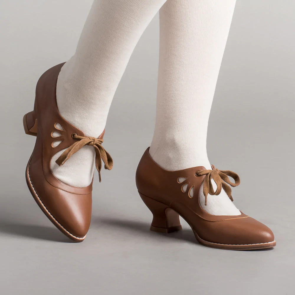 Braune Vintage-Damenschuhe mit Schnürung und Cut-Out-Details, getragen mit weißen Strumpfhosen. Retro-Design, eleganter Absatz, klassischer Stil.