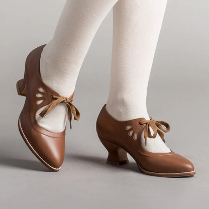 Braune Vintage-Damenschuhe mit Schnürung und Cut-Out-Details, getragen mit weißen Strumpfhosen. Retro-Design, eleganter Absatz, klassischer Stil.