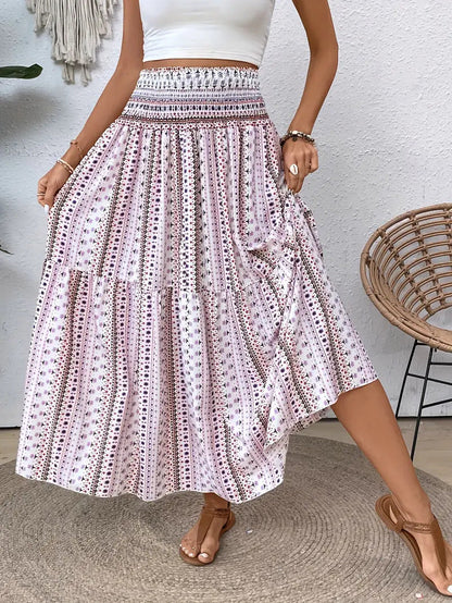Frau in weißem Crop-Top und langem, geblümtem Boho-Rock, steht neben einem Rattan-Stuhl. Sommermode, Boho-Stil, Freizeitkleidung.