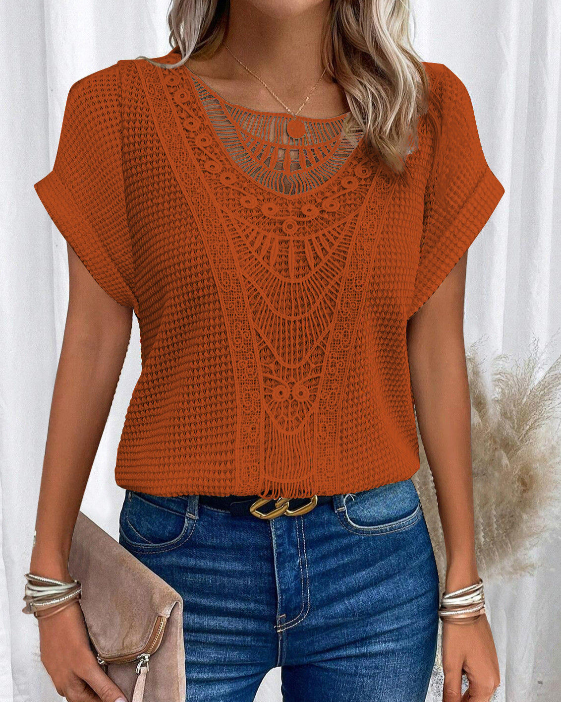 Frau in orangefarbener, gehäkelter Bluse und blauer Jeans, hält eine beige Clutch. Modetrend, Sommeroutfit, Damenmode, lässiger Stil.