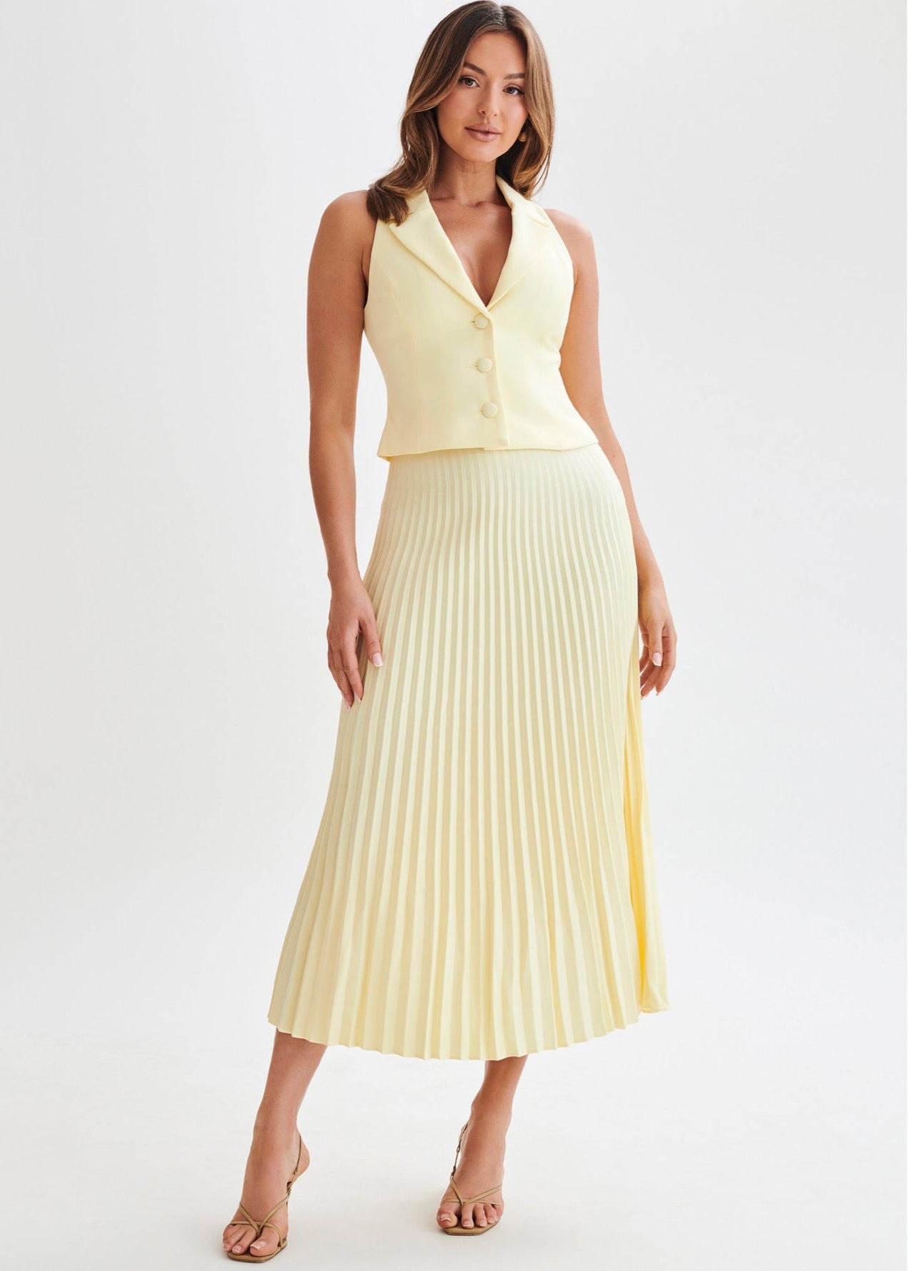 Frau in gelbem, ärmellosem Blazer und plissiertem Midirock, elegante Mode, Sommeroutfit, stilvolle Kleidung, modische Frau, Studioaufnahme.