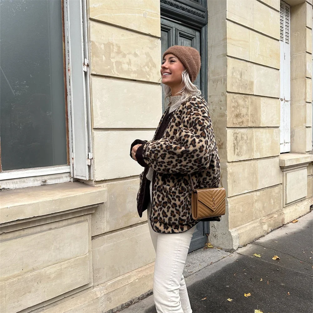 Frau in Leopardenmuster-Jacke und Mütze, steht lächelnd vor einem Gebäude. Modetrend Herbst, Streetstyle, beige Hose, braune Umhängetasche.