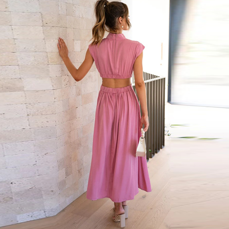 Frau in rosa Sommerkleid mit weißer Handtasche, steht an einer Steinwand. Elegante Mode, Freizeitkleidung, Rückansicht, modernes Design.