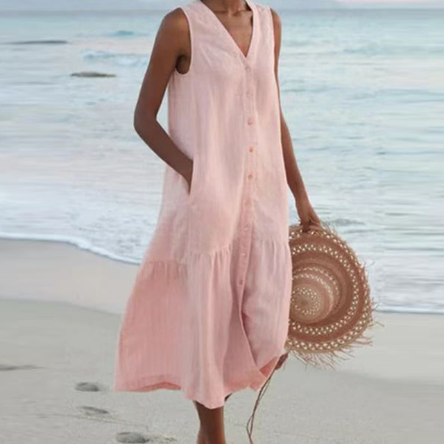 Frau in rosa Sommerkleid am Strand, hält runden Strohhut. Strandmode, Sommerkleid, Damenbekleidung, Urlaubsoutfit, Strandspaziergang.
