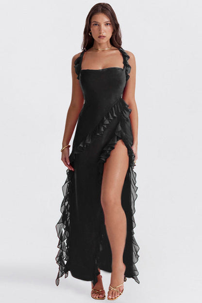 Frau in elegantem, schwarzem Abendkleid mit Rüschen und hohem Beinschlitz, trägt goldene Sandalen. Perfekt für formelle Anlässe und Modeevents.