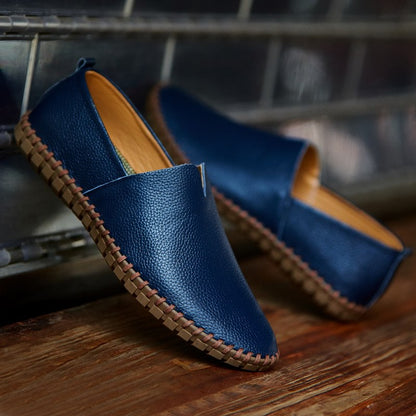 Blaue Lederschuhe mit brauner Sohle, lässig und modern, auf Holzboden vor Metallhintergrund. Perfekt für Herrenmode und Freizeitkleidung.